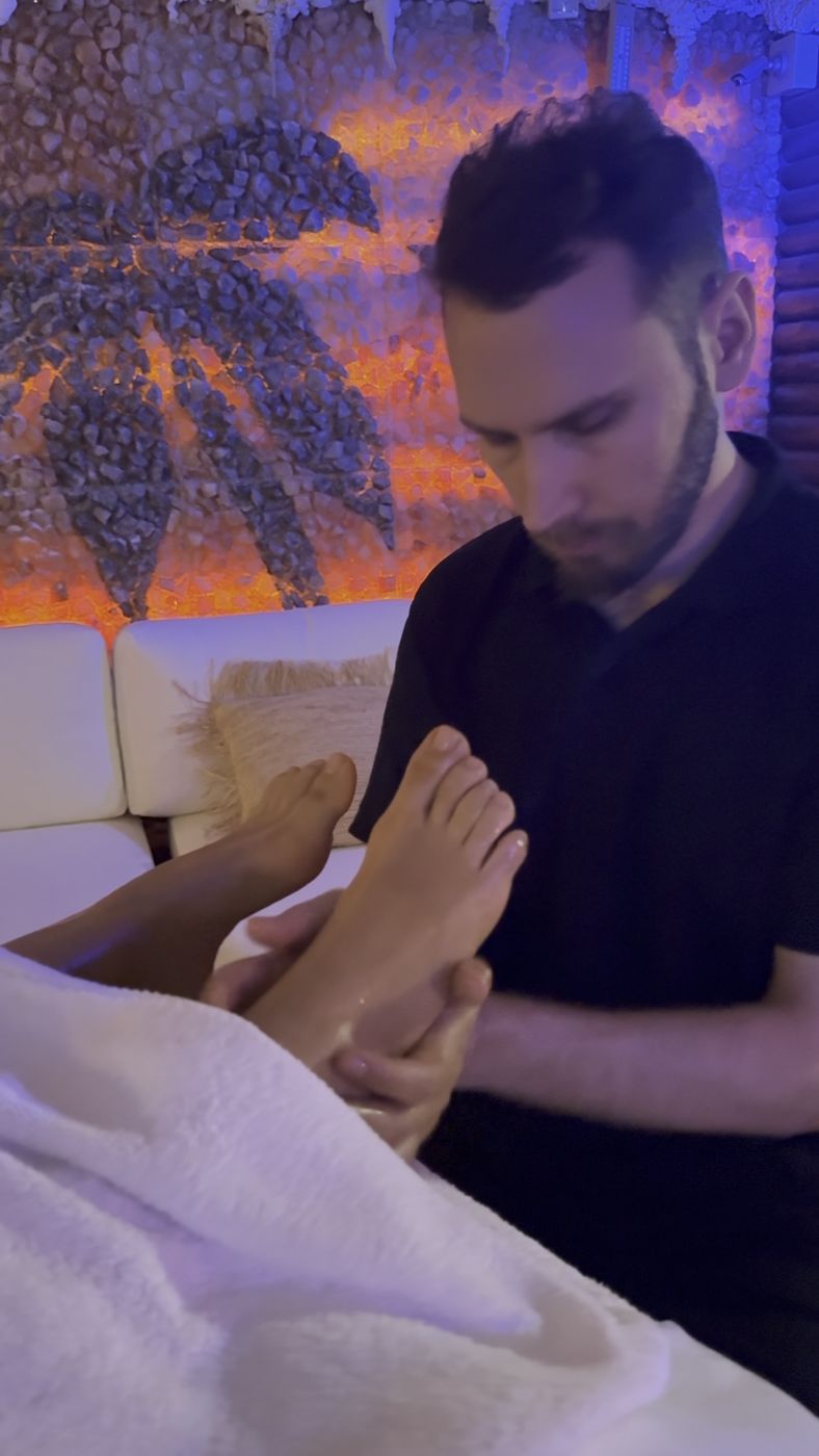 Sat Guru Charan — mani sui piedi del cliente durante la seduta, luce calda